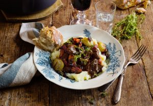 Klassisk Boeuf Bourguignon serverad på krämigt potatisstomp med steklök, morötter, knaprigt sidfläsk och ett glas rött vin.