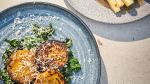 Grillade skivor av gulbeta på smörstekt svartkål, toppade med riven parmesan, på ett blått fat