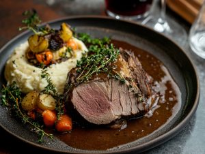 Skivad älgstek med gräddsås, potatispuré och rostade rotfrukter på en mörk tallrik, toppad med timjan