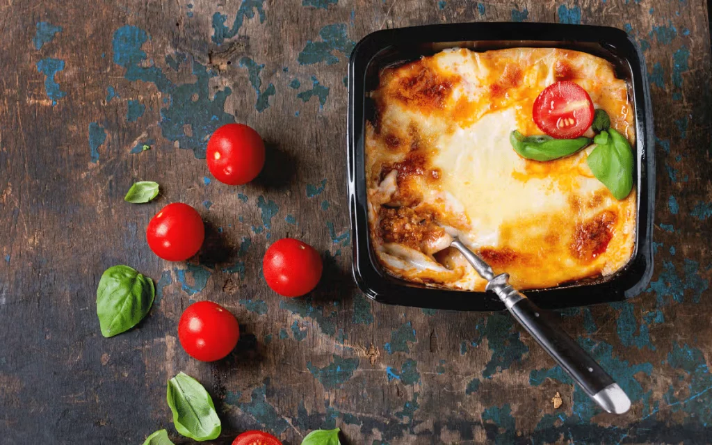 Klassisk lasagne al forno i form med gratinerad ost, basilika och färska tomater